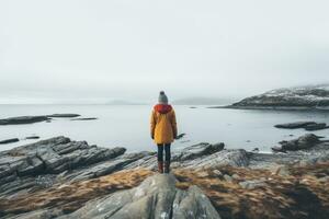 AI generated A young woman in a yellow raincoat stands on a rock and looks at the sea in the fog, Woman alone looking at foggy sea traveling adventure lifestyle outdoor solitude sad, AI Generated photo