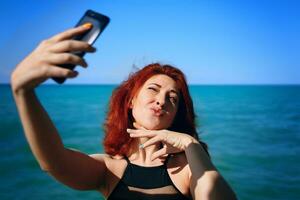 mujer pelirroja toma selfie en la cámara del teléfono inteligente. foto