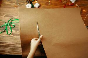 Las manos cortan una hoja de papel artesanal con unas tijeras. foto