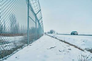 Private secured object near highway. Maximum security detention facility. Car goes on road. Barbed wire fence on border in winter. Closing for quarantine. Unauthorized entry is prohibited. photo