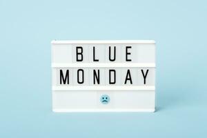 Blue monday concept. Light board with Blue monday text and sad face on blue background photo