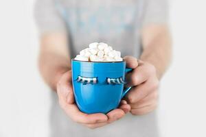 Man in gray t-shirt holds blue mug of hot chocolate with marshmallows. Blue monday concept photo