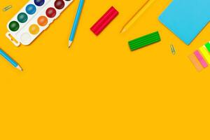 Watercolor paints, colored pencils, paper clips and notepad on yellow background. photo