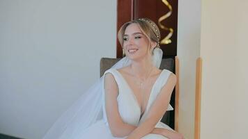 un' bellissimo sposa è seduta e guardare a il telecamera, sorridente Cordiali saluti. preparazione per il nozze giorno. contento sposa video