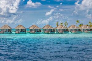 Aerial view of Maldives island, luxury water villas resort and wooden pier. Beautiful sky and ocean lagoon beach background. Summer vacation holiday and travel concept. Paradise aerial landscape pano photo