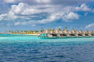 Aerial view of Maldives island, luxury water villas resort and wooden pier. Beautiful sky and ocean lagoon beach background. Summer vacation holiday and travel concept. Paradise aerial landscape pano photo