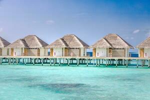 Aerial view of Maldives island, luxury water villas resort and wooden pier. Beautiful sky and ocean lagoon beach background. Summer vacation holiday and travel concept. Paradise aerial landscape pano photo