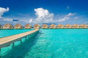 Aerial view of Maldives island, luxury water villas resort and wooden pier. Beautiful sky and ocean lagoon beach background. Summer vacation holiday and travel concept. Paradise aerial landscape pano photo