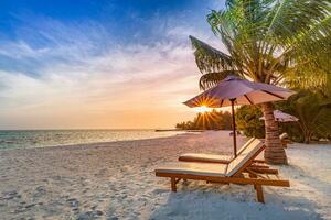 Beautiful tropical sunset scenery, two sun beds, loungers, umbrella under palm tree. White sand, sea view with horizon, colorful twilight sky, calmness and relaxation. Inspirational beach resort hotel photo