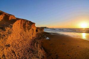 the sun sets over the ocean and sand dunes photo