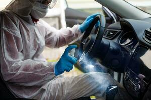 Cleansing car interior and spraying with disinfection liquid. Hands in rubber protective glove disinfecting vihicle inside for protection from virus disease photo