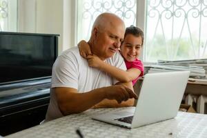 Granddaughter helping grandpa to make online communication on laptop photo