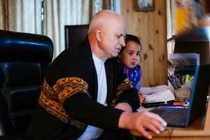 Granddaughter helping grandpa to make online communication on laptop photo