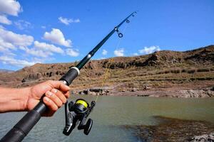 a person holding a fishing rod and reel on a lake photo