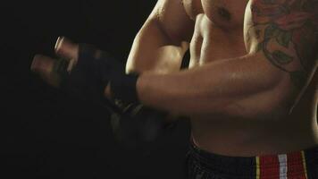 Ripped male boxer with sweaty torso taking off hand wraps after fighting video