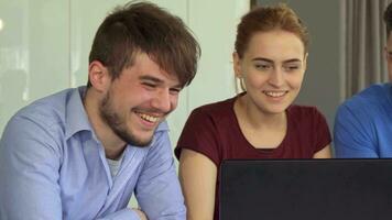 Young people laugh at the table with laptop video