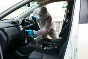 Disinfectant worker character in protective mask and suit sprays bacterial or virus in a car. photo