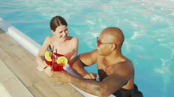 Happy multiethnic couple clinking glasses in the swimming pool video