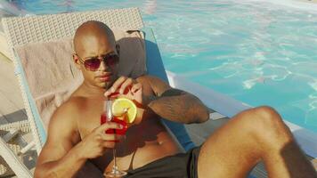 bonito homem bebendo coquetel banhos de sol às a à beira da piscina video