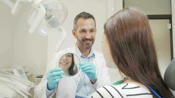 Cheerful mature dentist holding a mirror for his female patient video