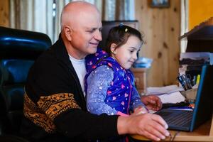 Granddaughter helping grandpa to make online communication on laptop photo