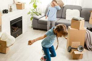 two little daughters celebrating moving day, excited by relocation into new house, laughing living room with cardboard boxes photo