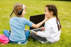 two funny schoolgirls sit on the grass and read books. Girls, girlfriends, sisters are taught lessons in nature. photo