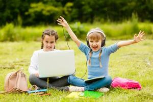 two funny schoolgirls sit on the grass and read books. Girls, girlfriends, sisters are taught lessons in nature. photo