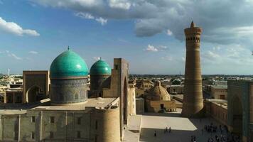 A drone flies over a group of tourists in front of the gates of the architectural complex PoiKalon in old Bukhara, Uzbekistan. Cloudy cloudy day. video