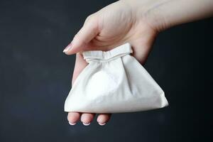 AI generated White fabric bag in female hand on dark background, close-up, A female hand close-up holding a small bag with white powder for sale, AI Generated photo