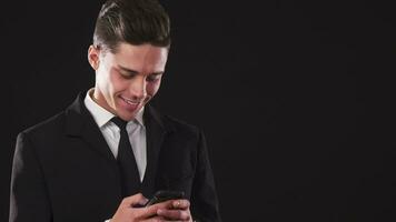 A smiling guy in a suit is typing something in his phone video