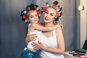 Beautiful young mother and her daughter with hair curlers photo