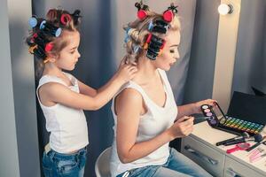 Beautiful young mother and her daughter with hair curlers photo