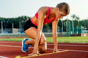 joven mujer atleta a comenzando posición Listo a comienzo un carrera en pista. foto