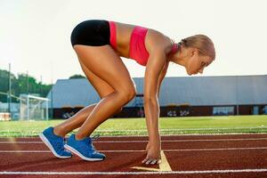 joven mujer atleta a comenzando posición Listo a comienzo un carrera en pista. foto