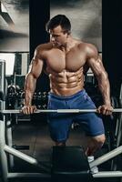 Handsome power athletic man on diet training pumping up muscles with dumbbell and barbell. Strong bodybuilder, perfect abs, shoulders, biceps, triceps and chest photo