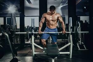 Handsome power athletic man on diet training pumping up muscles with dumbbell and barbell. Strong bodybuilder, perfect abs, shoulders, biceps, triceps and chest photo