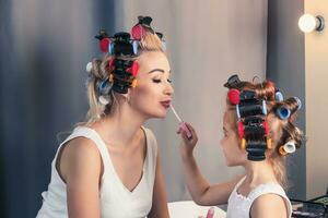Pretty mother and her daughter having fun with lipstick while photo
