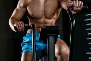 View close-up part of young man in sports shorts cycling at gym photo