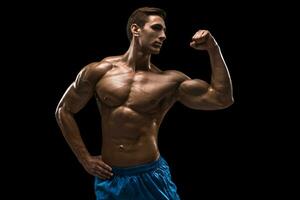 Muscular and fit young bodybuilder fitness male model posing over black background. photo