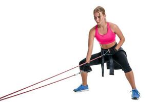 Strong woman using a resistance band in her exercise routine. Young woman performs fitness exercises on white background. photo