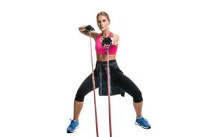 Strong woman using a resistance band in her exercise routine. Young woman performs fitness exercises on white background. photo