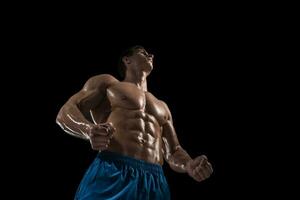 Muscular and fit young bodybuilder fitness male model posing over black background. photo