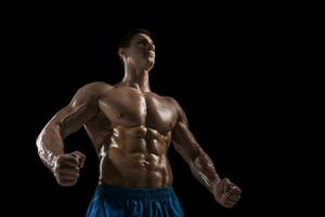 Muscular and fit young bodybuilder fitness male model posing over black background. photo