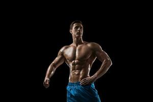 Muscular and fit young bodybuilder fitness male model posing over black background. photo