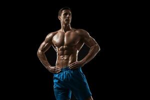 Muscular and fit young bodybuilder fitness male model posing over black background. photo