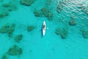 AI generated Aerial view of a woman kayaking in turquoise water, An aerial view of a woman on a surfboard in the turquoise waters of the Maldives, AI Generated photo