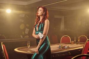 Young beautiful woman is posing against a poker table in luxury casino. photo