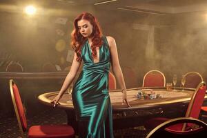 Young beautiful woman is posing against a poker table in luxury casino. photo