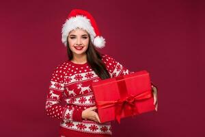 Young beautiful woman holding Christmas present in her hands on red studio background photo